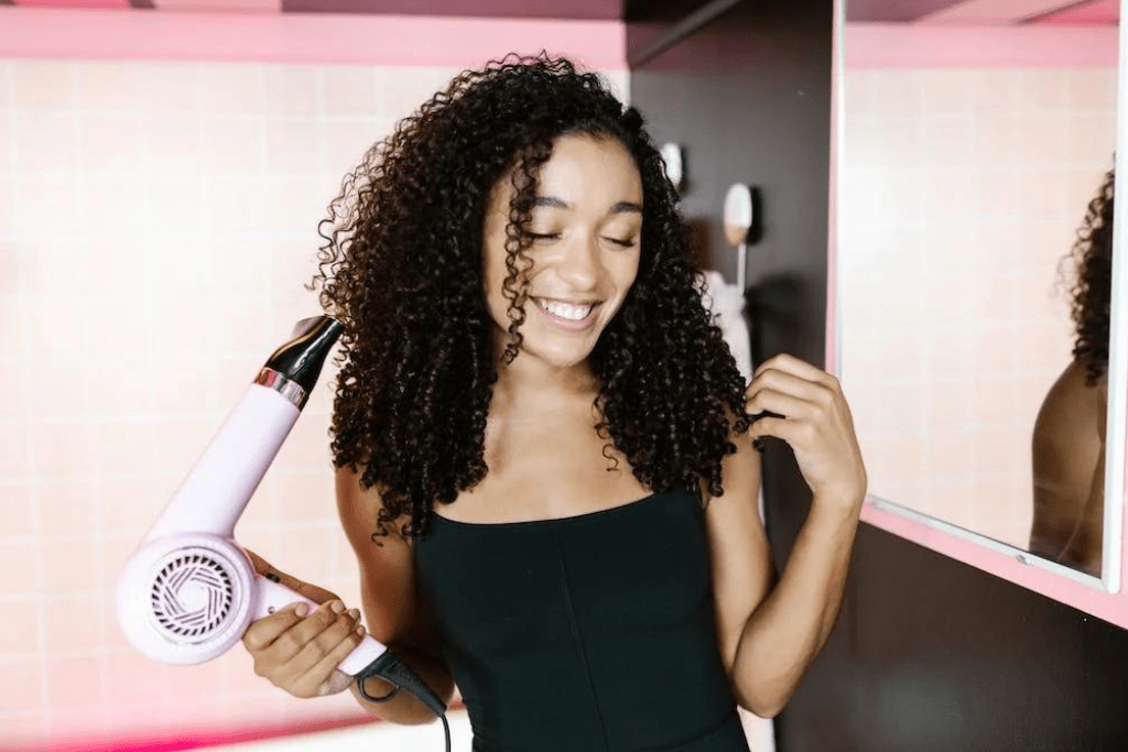 Women with curly hair holding pink hair dryer 