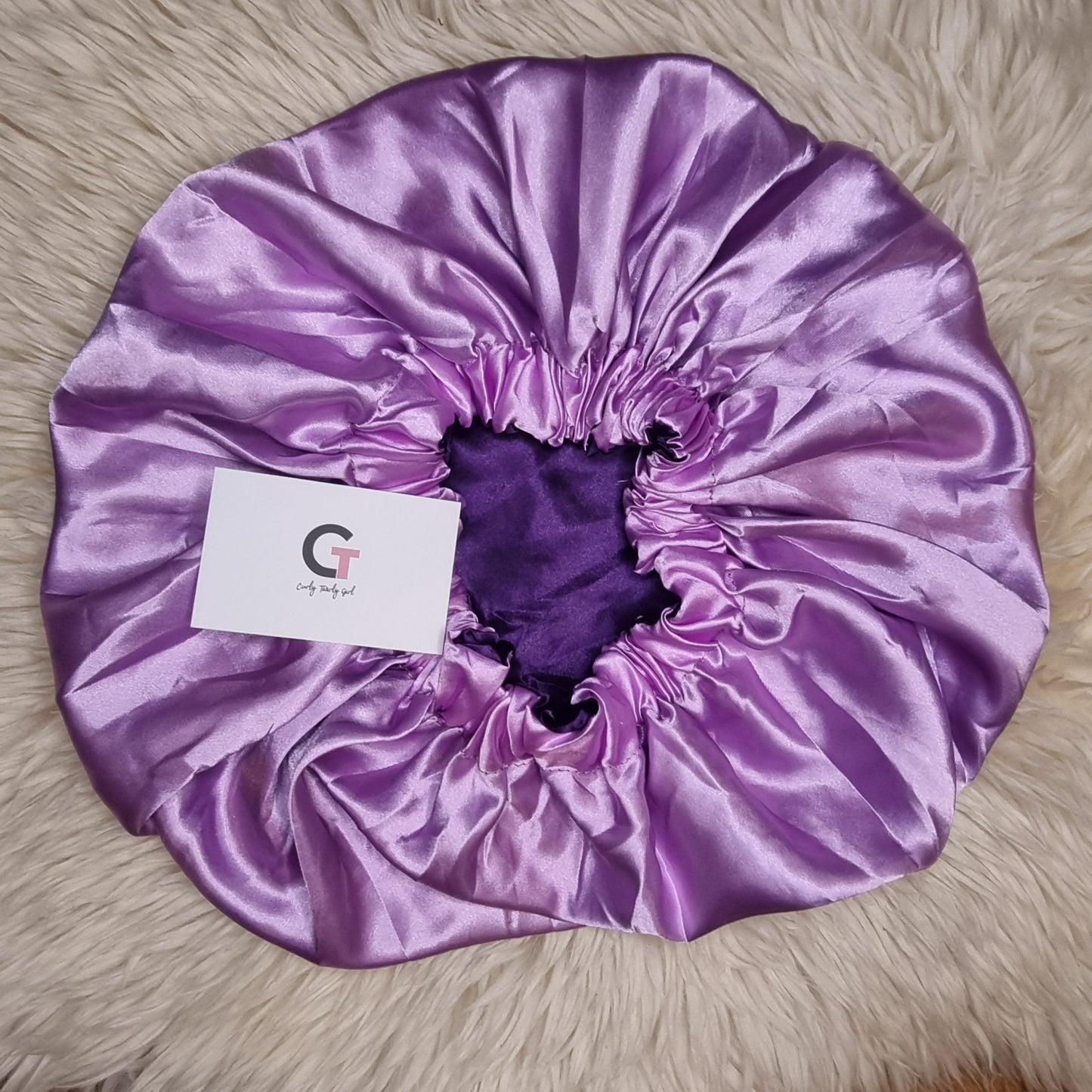 Curly Twirly Girl purple reversible satin bonnet on cream rug