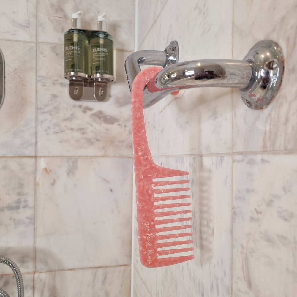 Pink wide tooth shower comb with handle hanging in shower